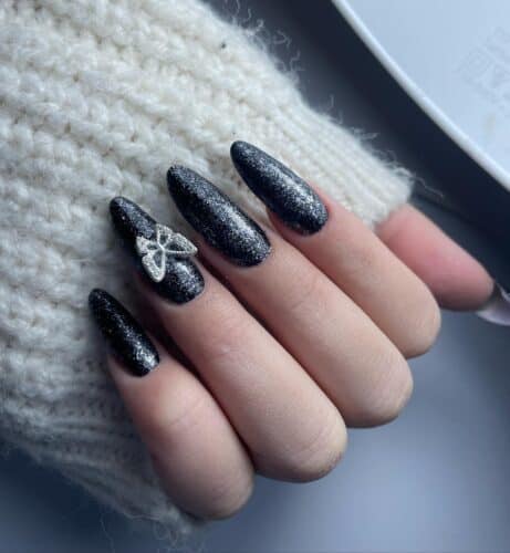 Black nails with a sparkling finish and a delicate butterfly embellishment, evoking the beauty of a starry night sky.