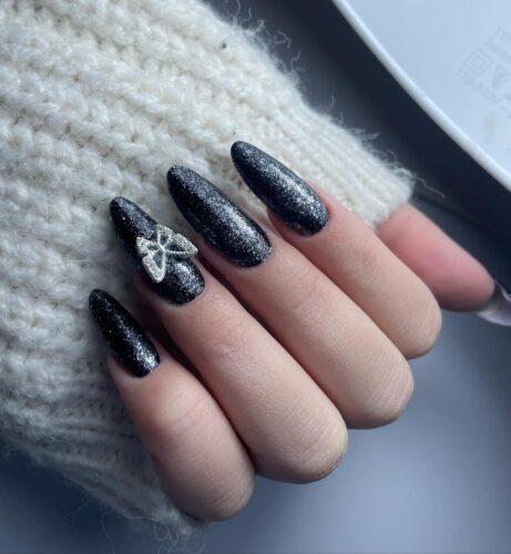 Black nails with a sparkling finish and a delicate butterfly embellishment, evoking the beauty of a starry night sky.