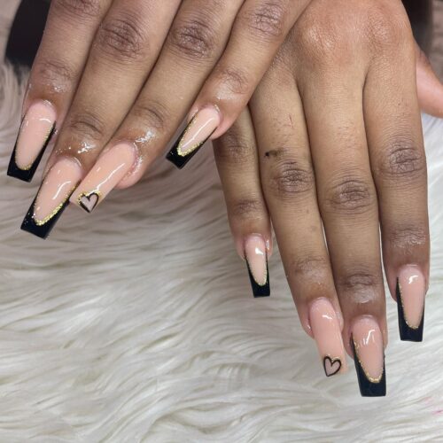 Glossy black French tips with gold and black heart accents on a natural nail base.