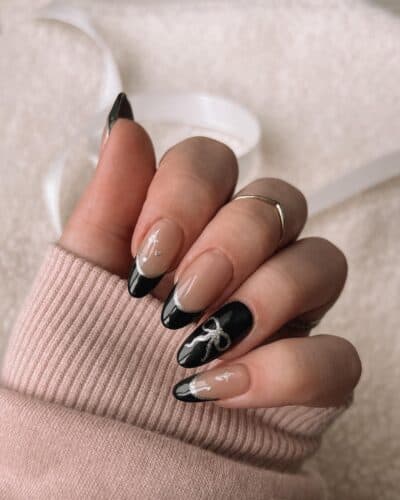 Black and silver glitter French tip nails with a nude base and bow designs.