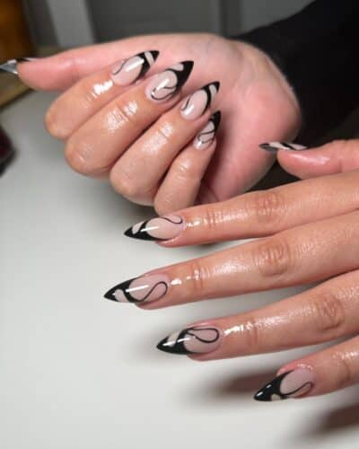 Nude nails with abstract black French tip designs featuring whimsical lines and shapes.