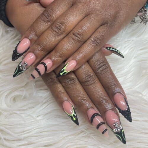 Stiletto nails with black French tips, featuring intricate designs and neon green accents.