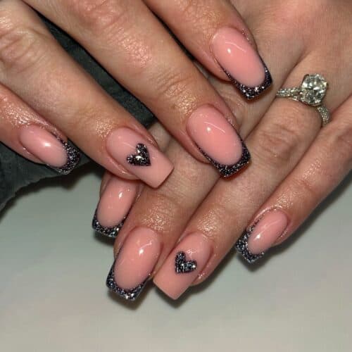 Square nails with black French tips featuring glitter outlines and small heart decals.