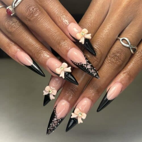 Stiletto nails with black French tips, corset patterns, and flower decorations enhanced with small gems.
