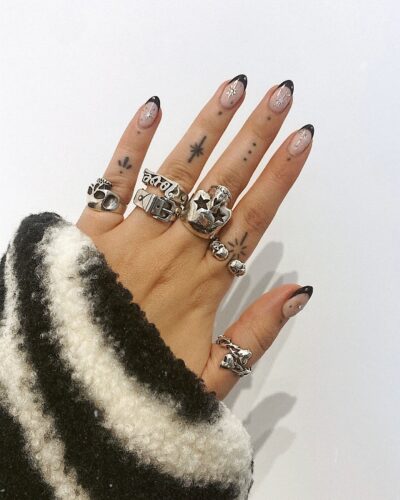 Oval nails with black French tips and silver celestial designs, including stars and abstract patterns.