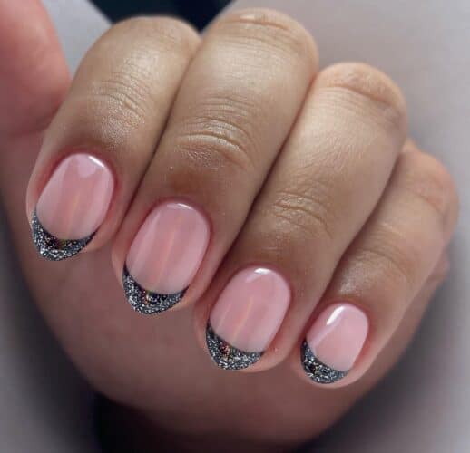 Round nails with black French tips accented by a crescent of sparkling silver glitter.