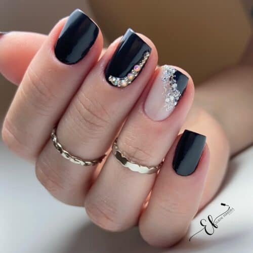 Short nails painted in glossy black with accent nails featuring a gradient of sparkling crystals and glitter.
