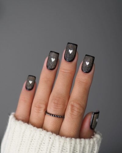 Square-shaped French nails with a textured black glitter surface and a single white heart on each nail.