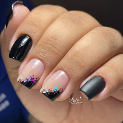 Glossy and matte black nails featuring a vibrant, multicolored glitter French tip on two nails for a festive look.