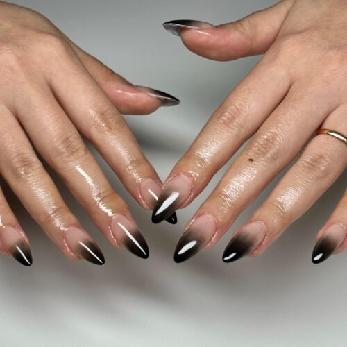 Almond-shaped nails with a seamless ombre transition from translucent nude to deep black at the tips.