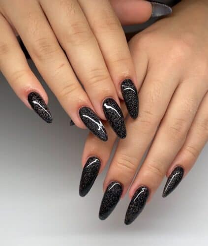 Long, almond-shaped nails with a glittery black finish that sparkles like a starry night.