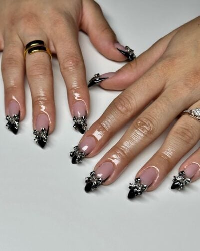 Long stiletto nails with glossy black tips and dramatic silver bow accents for a bold look.