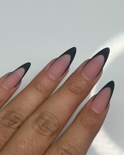 Long stiletto nails with a sharp black French tip against a nude base.