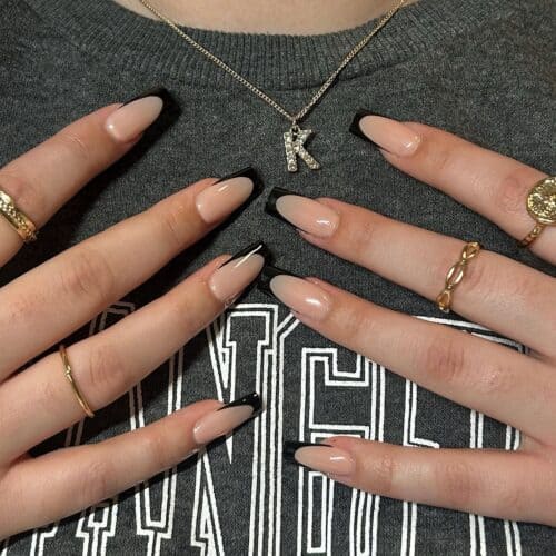 Coffin-shaped nails with black French tips and a monogram detail, adorned with gold rings.