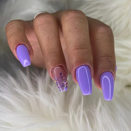 Vibrant purple nails with one finger adorned in sparkling purple glitter, showcasing playful luxury.