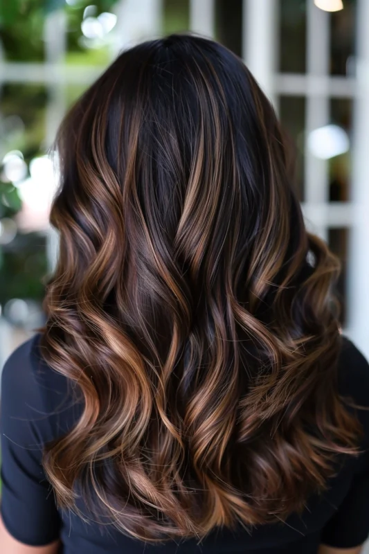 Back view of dark brown hair cascading in waves, highlighted with rich caramel tones.