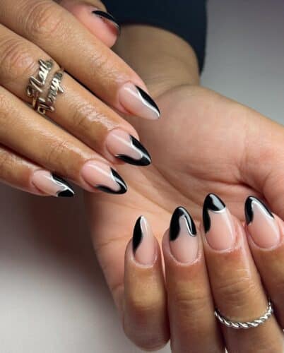 Oval nails with sleek black French tips enhanced by artistic silver swirl designs.