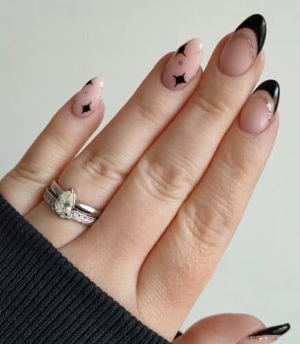 Nude nails with playful black French tips featuring small star and moon silhouettes.