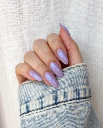 Long almond-shaped nails with a soft lavender hue and a pearlescent finish on a denim fabric background.