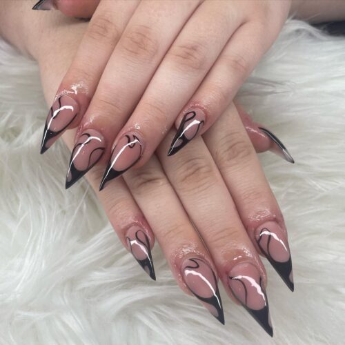 Long nails with sharp black French tips over a nude base, offering a bold and edgy look.