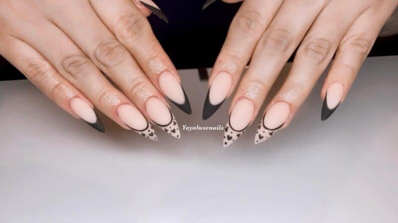 Nude matte nails with black French tips and whimsical tiny hearts for a playful look.