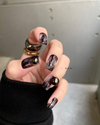 Long nails with a smoky black marble design and a single gold rivet for an elegant and luxurious look.