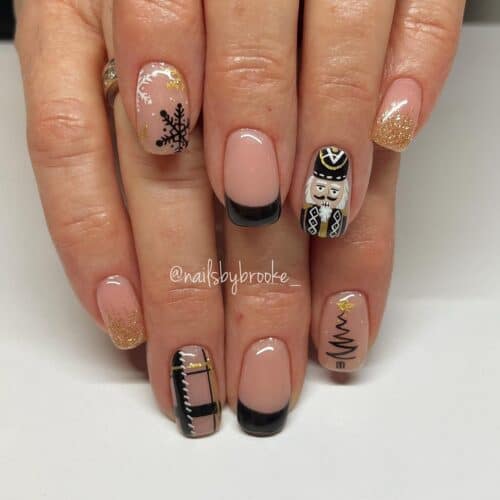 A variety of nail designs including a Nutcracker character, snowflakes, and golden glitter, all incorporating black French tips.