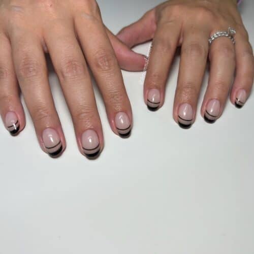 Nude nails with sharply defined black French tips with double lines, showcasing a modern and elegant design.