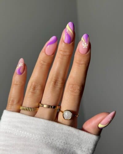 Almond-shaped nails with lavender and yellow swirls and a small white flower design on a cozy white sleeve.