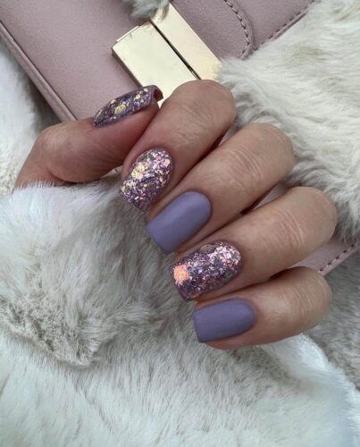 Matte lavender nails with accent nails covered in gold and purple glitter flakes.