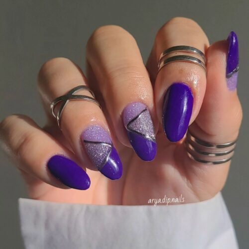 Almond-shaped nails with various purple shades and a distinct purple glitter design against a soft grey background.