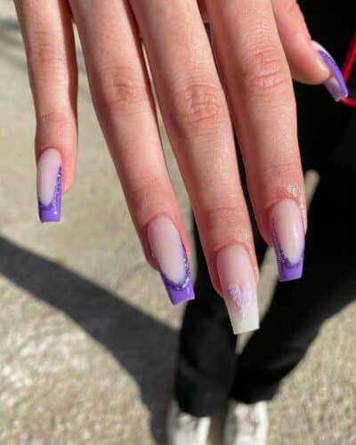 Coffin-shaped nails with sheer bases, purple tips, subtle glitter accents, and small heart decals.