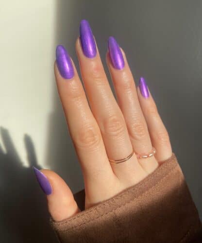 Long, pointed stiletto nails painted in a shiny, deep purple color.