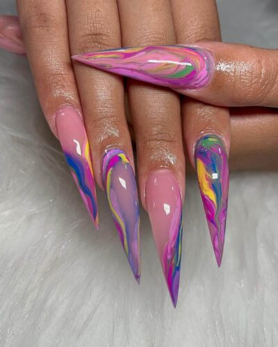 Stiletto-shaped nails with a vibrant purple base and a creative swirl design in pink, blue and yellow, capturing the joy of summer.