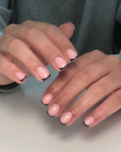 Short nails with a nude base and thin black French tips, embodying minimalist elegance.