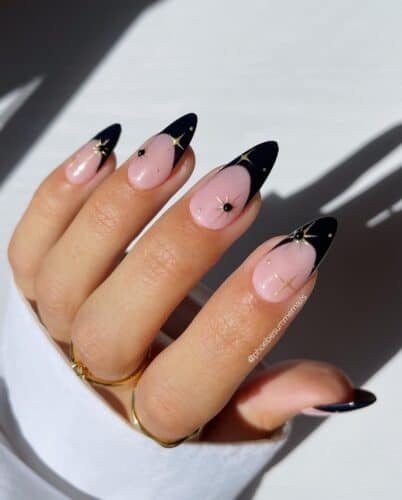 Stiletto nails with black French tips and delicate golden stars, adding a touch of celestial elegance.