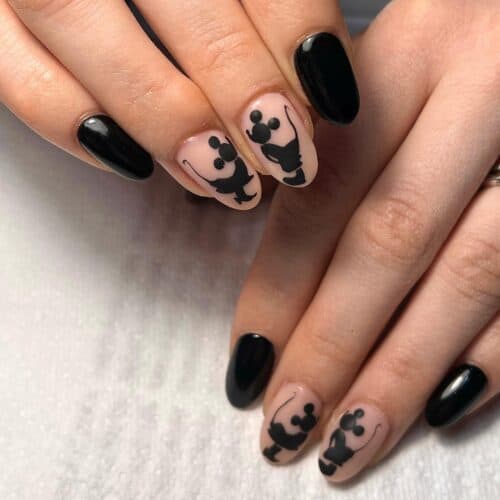 A person's hands with nails painted in glossy black and nude, featuring playful black silhouette art on the nude nails.