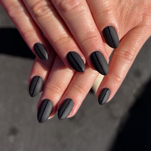 Hands with short nails coated in a luxurious matte black polish, exuding understated elegance.