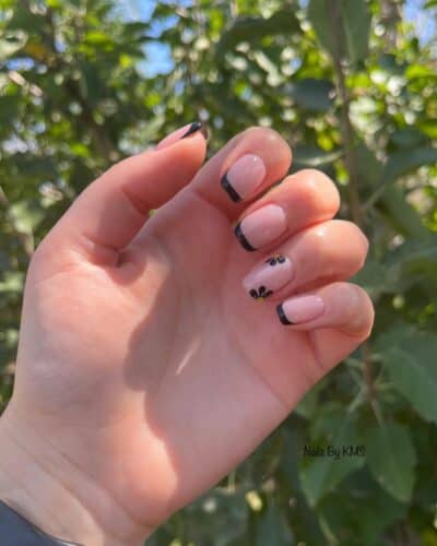 Short nails with classic black French tips and a single nail featuring a delicate floral design, evoking the whimsy of nature.