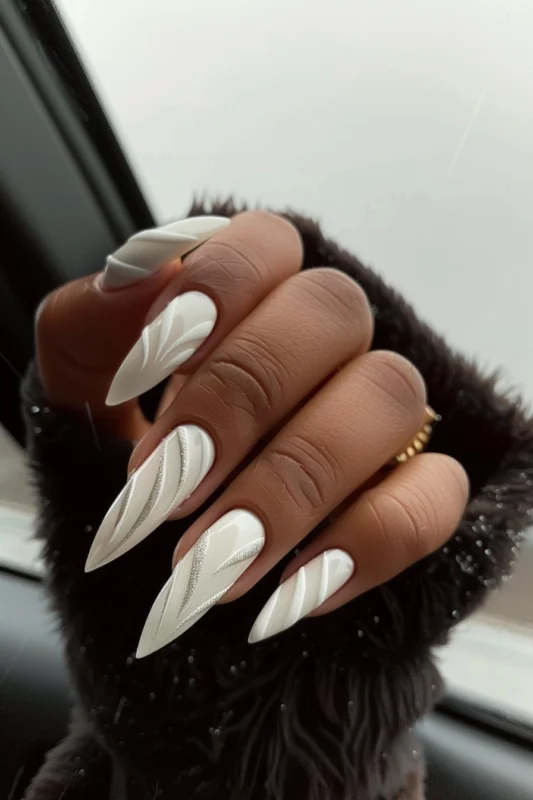 Milky white stiletto nails with artistic white and silver swirls.