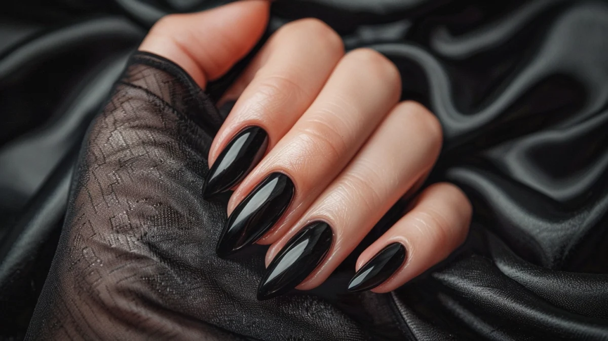 A woman's hand showcasing glossy black nail polish on long, almond-shaped nails.