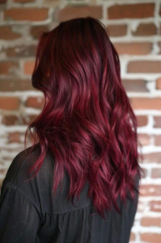 A woman's long, curly merlot red hair against a brick background.