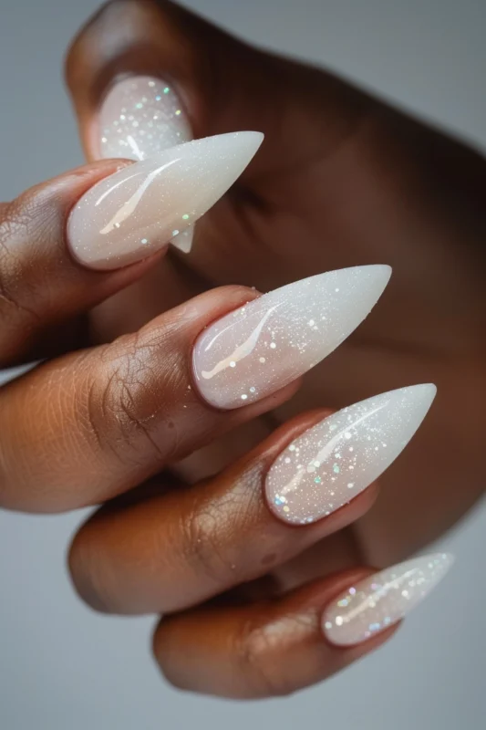 Stiletto nails with a milky base covered with glitter.