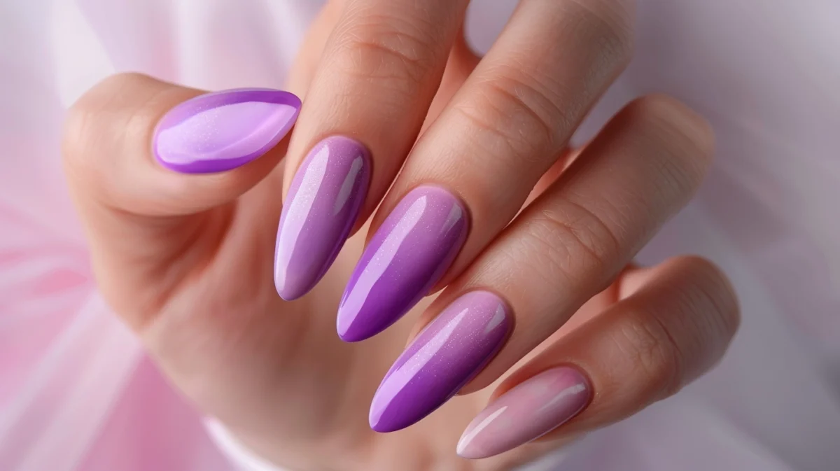 A woman's hand showcasing a manicure with pastel purple and light pink nail polish on long, almond-shaped nails.