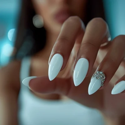 Woman showing off white nails with rhinestones detail.