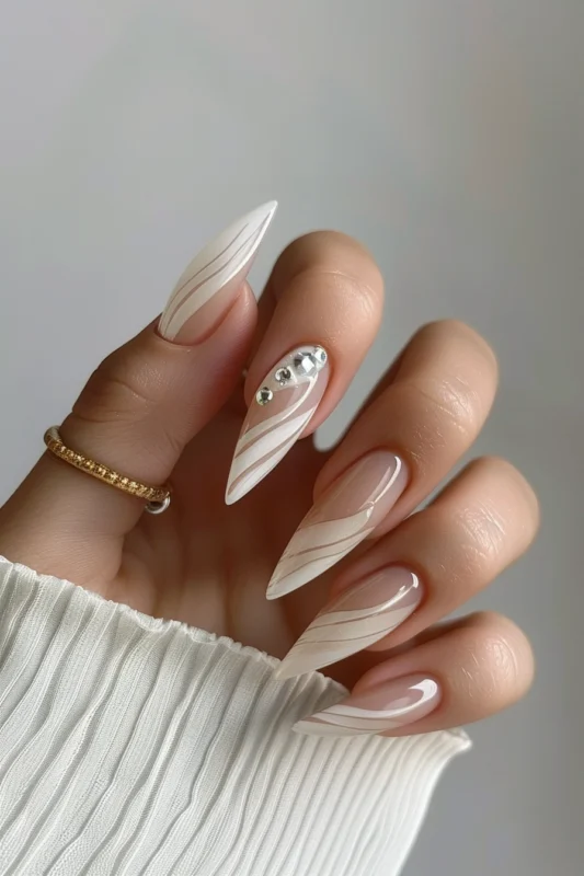 White and clear stiletto nails with a leafy design and rhinestone accents.