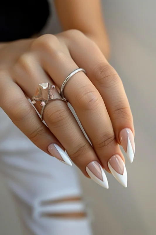 Stiletto nails with a nude base and a sharp geometric white tip.