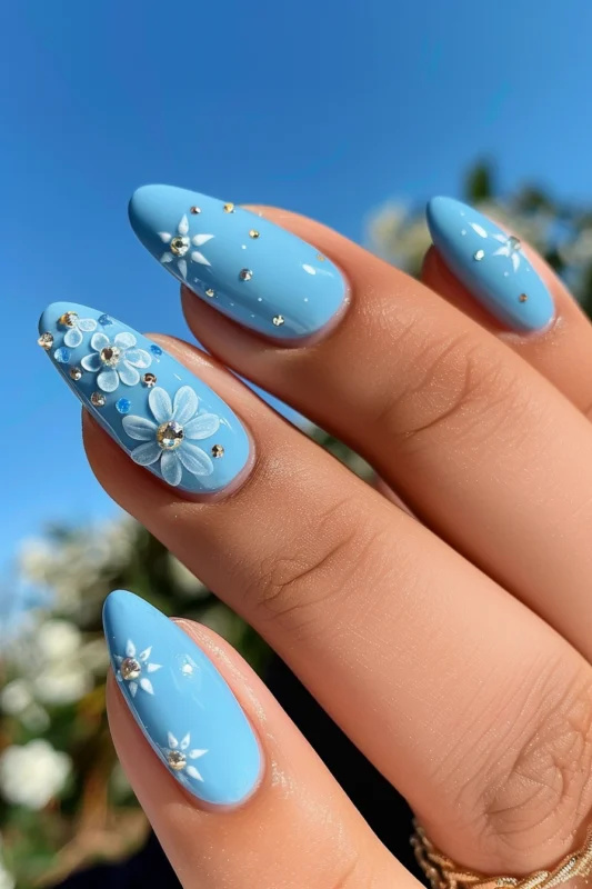 Baby blue almond nails with flower designs and gem accents.