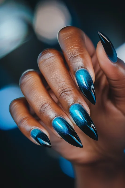 Stiletto nails with a blue to black ombre and metallic finish.
