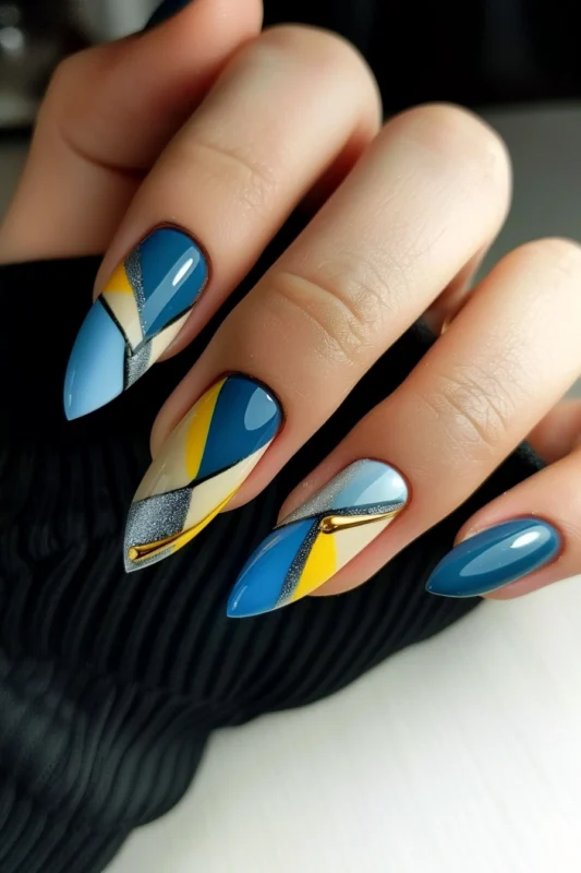 Stiletto nails with blue, yellow, and metallic geometric patterns.